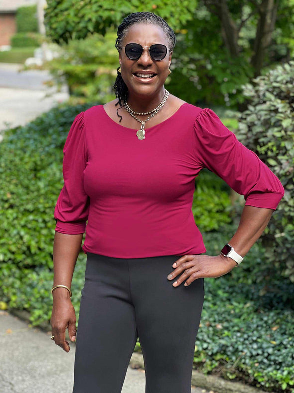 Miik model Pat (five feet eight, large) smiling while wearing Miik's Gigi reversible puff sleeve blouse in bordeaux with a graphite pant and sunglasses