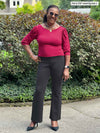 Miik model Pat (five feet eight, large) smiling standing in a sidewalk while wearing Miik's Gigi reversible puff sleeve blouse in bordeaux with a graphite pant and sunglasses