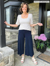Miik founder Donna (five feet six, small) standing in front of a house smiling wearing a navy capri pant with Miik's Gigi reversible puff sleeve blouse in cobblestone print