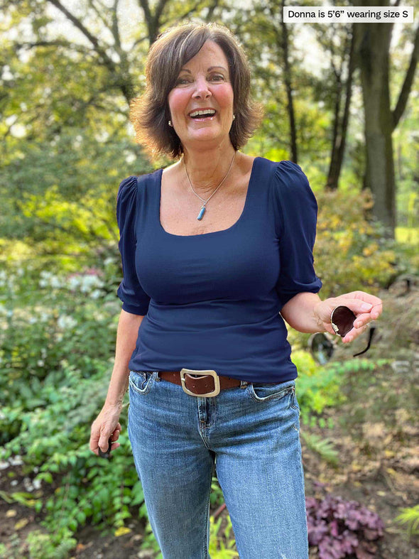 Woman standing in nature wearing Miik's Gigi reversible puff sleeve blouse in navy with jeans.
