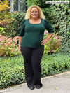 Woman standing in nature wearing Miik's Gigi reversible puff sleeve blouse in pine green with pants.