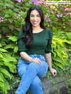 Woman sitting in nature wearing Miik's Gigi reversible puff sleeve blouse in pine green with jeans.