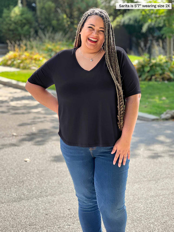 Miik plus size model Sarita (5'7", 2x) smiling wearing Miik's Gracelyn v-neck classic tee in black with jeans