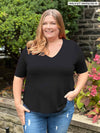 Miik plus size model Kelly (5'7", 3x) smiling and looking away wearing Miik's Gracelyn v-neck classic tee in black with jeans