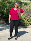Miik plus size model Sarita (5'7", 2x) smiling wearing a black legging along with Miik's Gracelyn v-neck classic tee in bordeaux