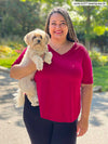 Miik plus size Sarita (5'7", 2x) smiling while holding a puppy wearing Miik's Gracelyn v-neck classic tee in bordeaux