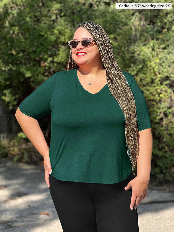 Miik plus size model Sarita (5'7", 2x) smiling and looking away wearing Miik's Gracelyn v-neck classic tee in pine green with a legging in black