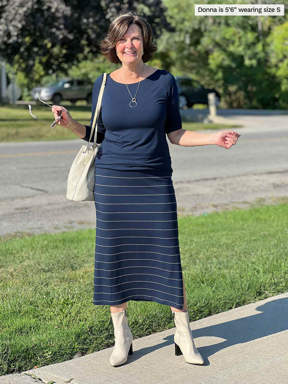 Miik founder Donna (five feet six, small) smiling wearing Miik's Hilden ballet top in navy along with a midi skirt in the same colour but pinstripe, boots and a shoulders purse 