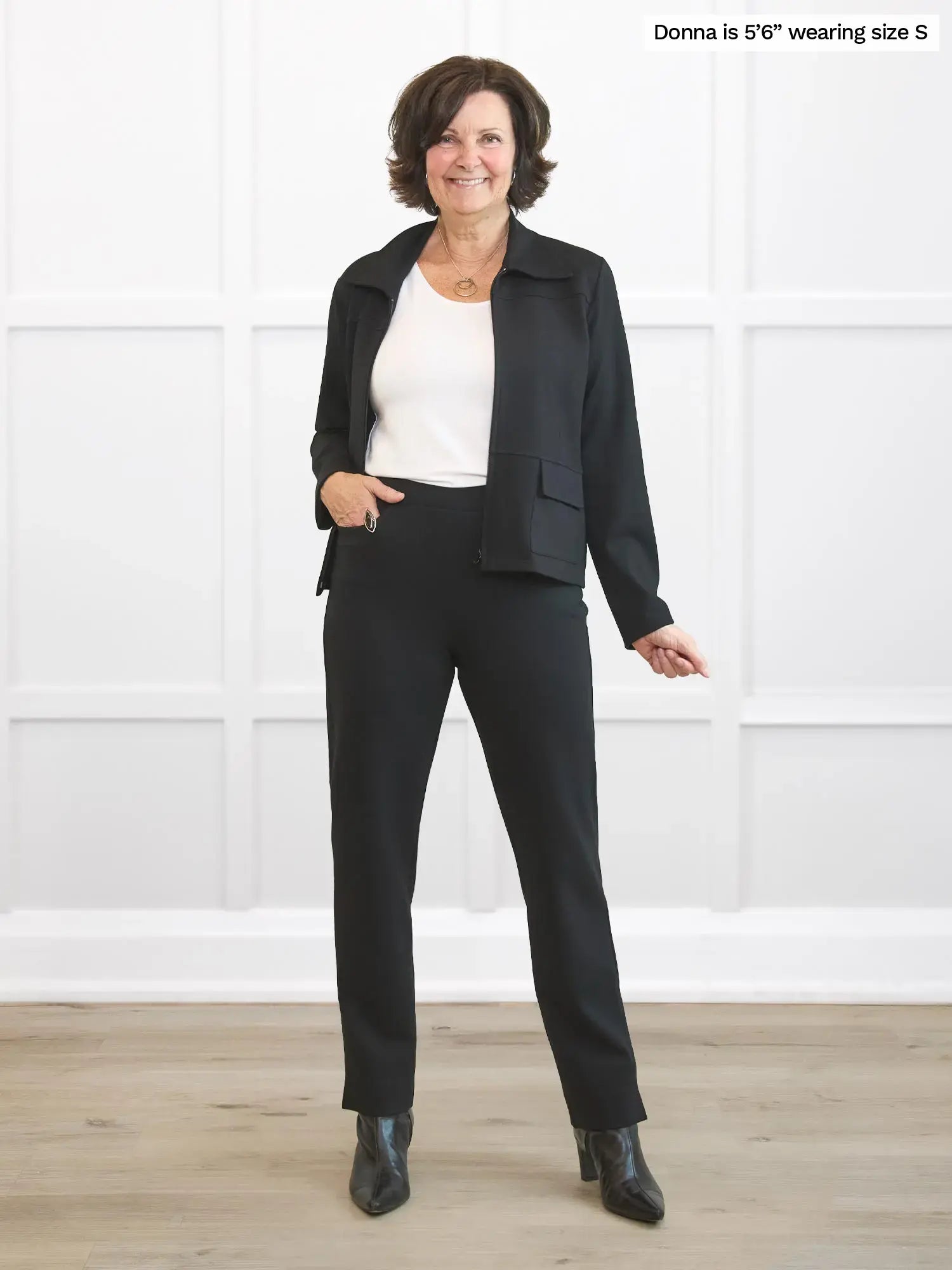 Woman wearing a black suit standing against a white wall. 