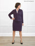 Woman wearing a purple suit standing against a white wall. 