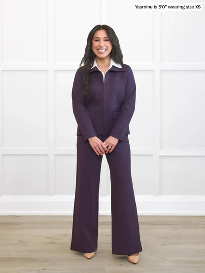 Woman wearing a purple outfit with a white shirt against a white wall. 