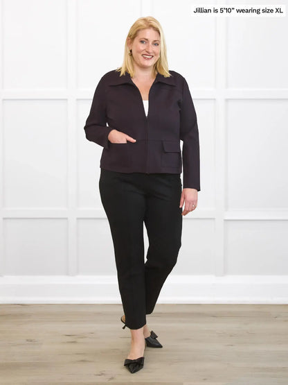 Woman wearing a dark brown and black outfit standing against a white wall. 