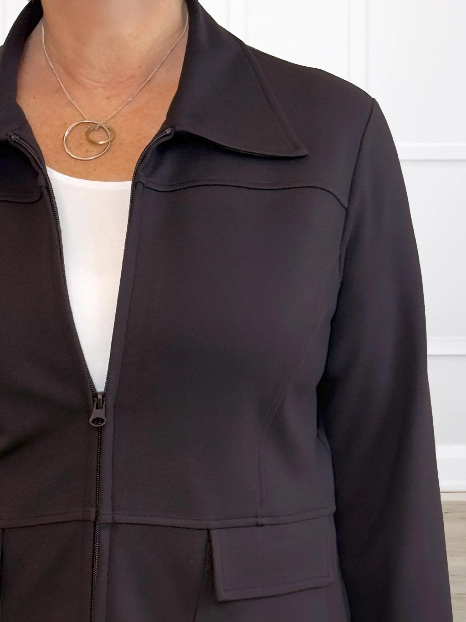Dark brown jacket worn over a white shirt with a necklace, against a neutral background 