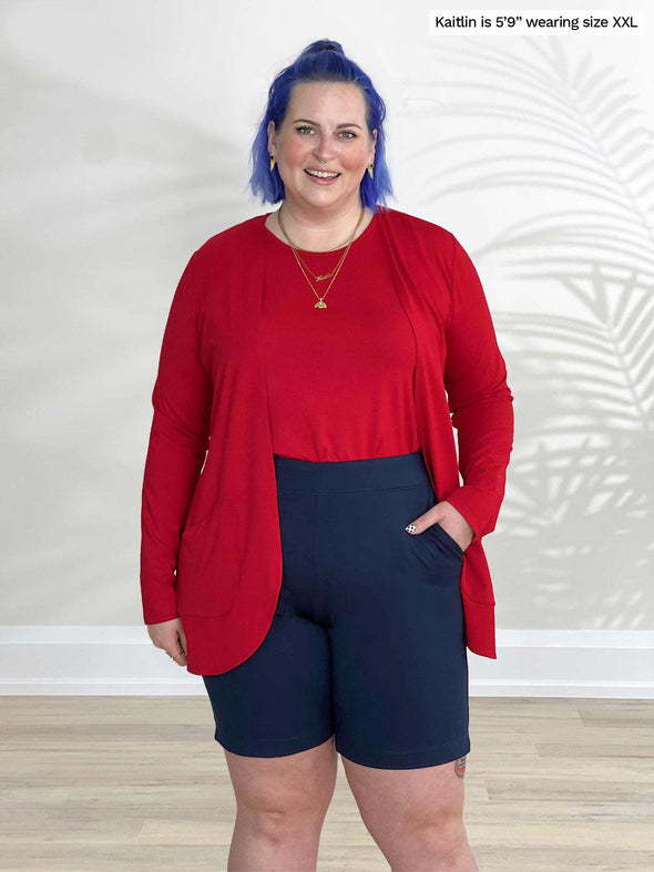 Miik model Kaitlin (5'9", xxlarge) smiling wearing Miik's Irelynn bermuda pocket short in navy with a poppy red tank with a cardigan in the same colour 