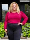 Miik model Carley (5'2", xxlarge) smiling wearing Miik's Janette puff sleeve reversible blouse in red wine tucked in a black pant