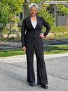 Miik model Keethai (5'5", medium) smiling wearing a black suit: Miik's Jeremy high waisted wide leg ponte pant along with Emily soft blazer and a collared white shirt 
