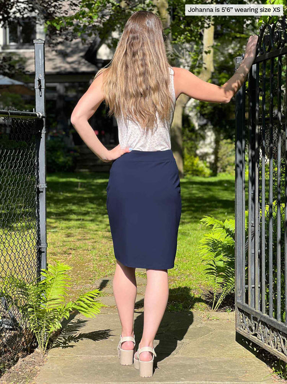 Miik model Johanna (five feet six, size xsmall) standing with her back towards the camera showing the back of Miik's Jilly mid-rise pull on skirt in navy