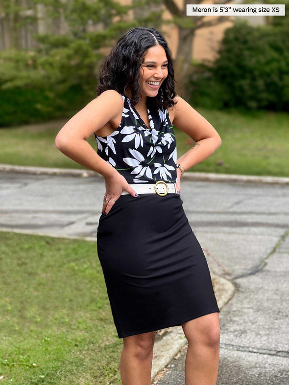 Miik model Meron (5'3", xsmall) laughing standing sideway wearing Miik's Jilly pull-on pencil skirt in black with a white belt and a printed top 