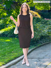Miik model Yasmine (5'0 - xsmall - petite) smiling holding a purse on her arm wearing Miik's Jilly pull-on pencil skirt in dark chocolate along with a tank top in the same colour 