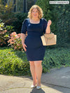 Miik model Bri (5'5 - xlarge) smiling while standing in front of a garden wearing Miik's Jilly pull-on pencil skirt in navy with a blouse in the same colour
