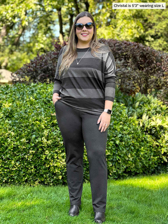 Miik model Christal (5'3", large) smiling wearing Miik's Kallyn slouchy dolman long sleeve top in dark ash stripe and a charcoal pant