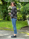 Miik founder Donna (5'6", small) standing sideway smiling wearing Miik's Kallyn slouchy dolman long sleeve top in dark ash stripe, jeans and black shoes