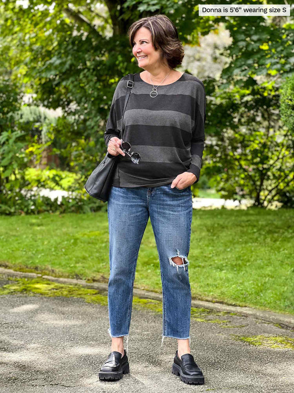 Miik founder Donna (5'6", small) looking away wearing Miik's Kallyn slouchy dolman long sleeve top in dark ash stripe, ripped jeans and black accessories 