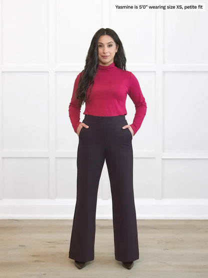 Woman wearing a pink turtleneck and dark brown petite pants against a white background 
