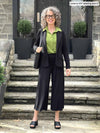Miik model Liane (5'9", small) smiling wearing Miik's Keethai wide leg culotte in black along with a blazer in the same colour and a collared shirt in green moss 