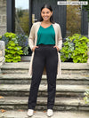 Miik model Meron (5'3", xsmall) smiling with hans on pockets wearing Miik's Keltie ponte mid-rise slim pant in black with a jade melange tee and a long cardigan in camel melange 