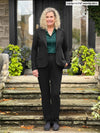 Miik model Carolyn (5'10", large, tall) standing on a door way wearing Miik's Keltie ponte mid-rise slim pant in black with a matching colour blazer and a green pine collared shirt