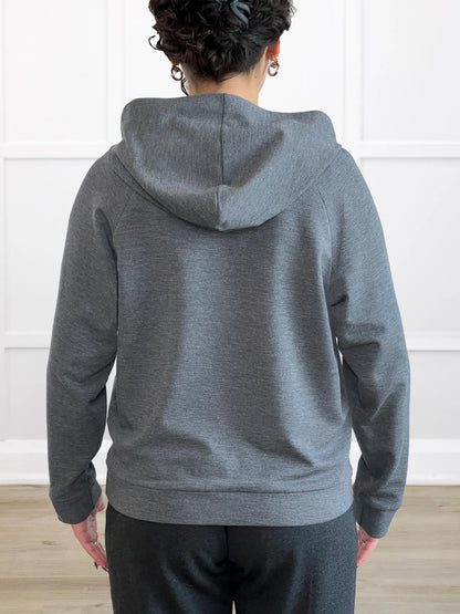 Person wearing a gray hoodie from behind with a white wall background 