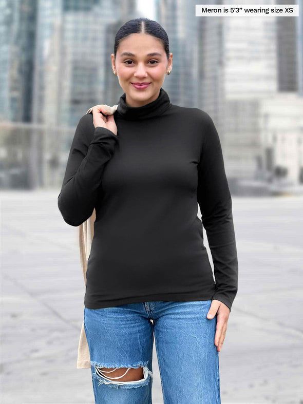 Woman standing in the street wearing Miik's Kerry turtleneck top in black with jeans.