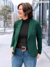 Woman standing in the street wearing Miik's Kerry turtleneck top in black with jeans and a blazer overtop