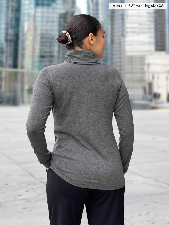 Miik model Meron (5’3”, xsmall) standing with her back towards the camera showing the back of Miik's Kerry turtleneck top in granite melange 