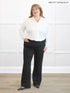Woman wearing a white blouse and black pants against a white background 