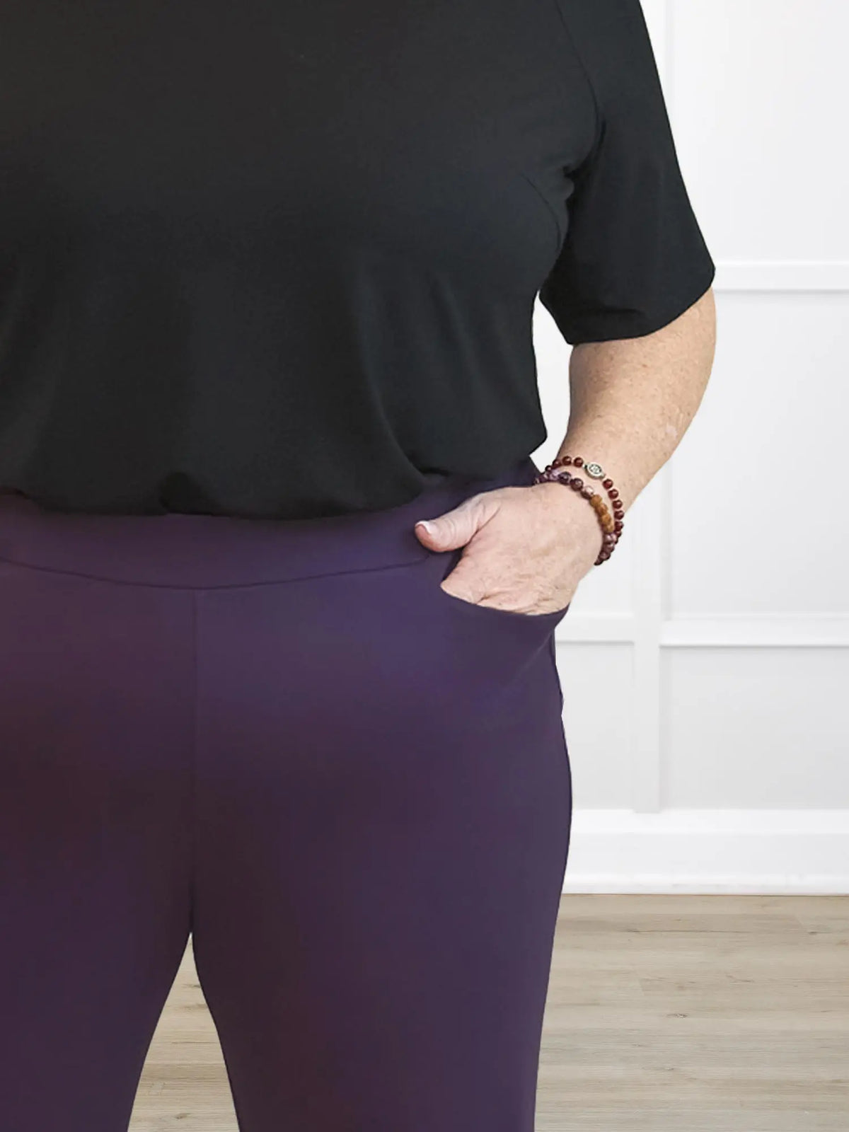 Person wearing a black top and purple pants with a white wall background 