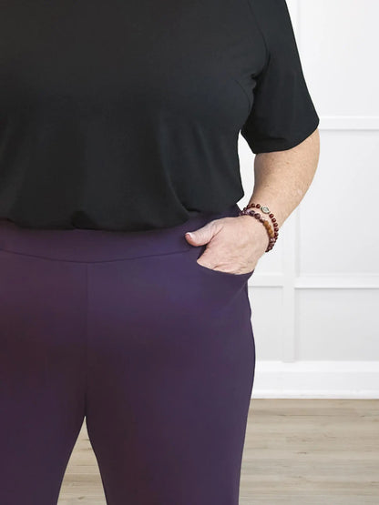 Person wearing a black top and purple pants with a white wall background 