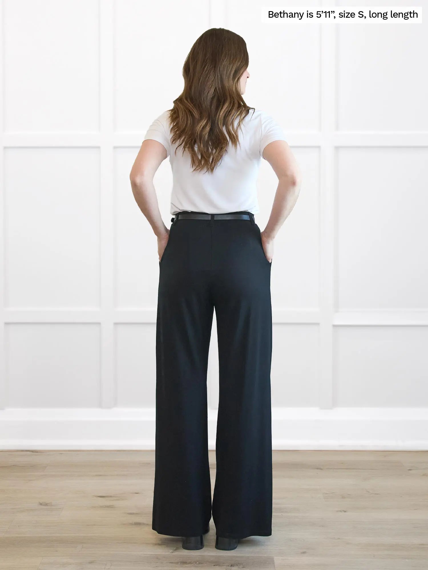 Woman wearing black wide-leg pants and a white top against a white wall 