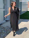 Miik founder Donna (five feet six, small) walking in front of a building looking away wearing Miik's Lina midi knot dress in black with a leather jacket on her shoulders and black boots 