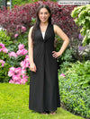 Miik model Yasmine (five feet tall, xsmall, petite) standing next to a garden wearing Miik's Lina midi knot dress in black and a white top underneath it 