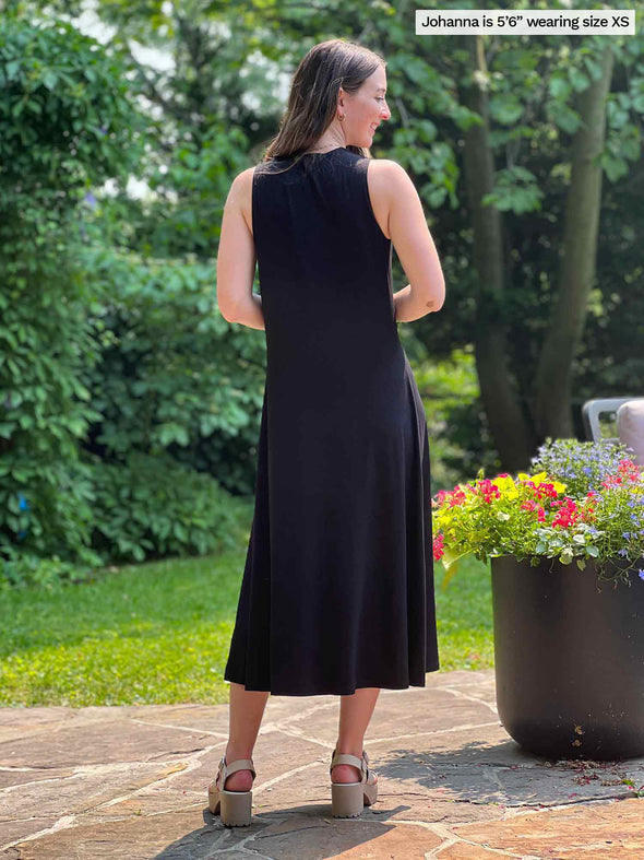 Miik model Johanna (five feet six, size xsmall) standing with her back towards the camera showing the back of Miik's Lina midi knot dress in black