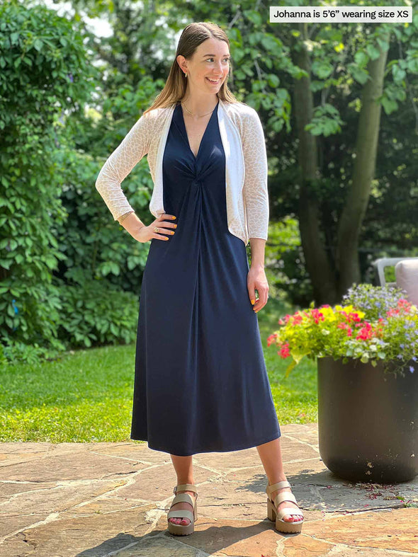 Miik model Johanna (five feet six, xsmall) smiling while looking away wearing Miik's Lina midi knot dress in navy with a cropped cardigan in cobblestone print