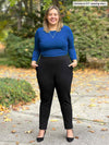 Miik model Christal (5'3", large) smiling with both hands on pockets wearing Miik's Linaya luxe fleece jogger in black with a blueberry long sleeve top tucked in