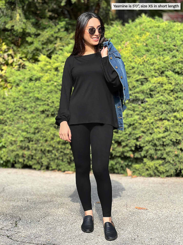 Miik model Yasmine (5'0", xsmall, petite) smiling and looking away wearing Miik's Lisa2 high waisted legging short length in black along with a long sleeve top in the same colour
