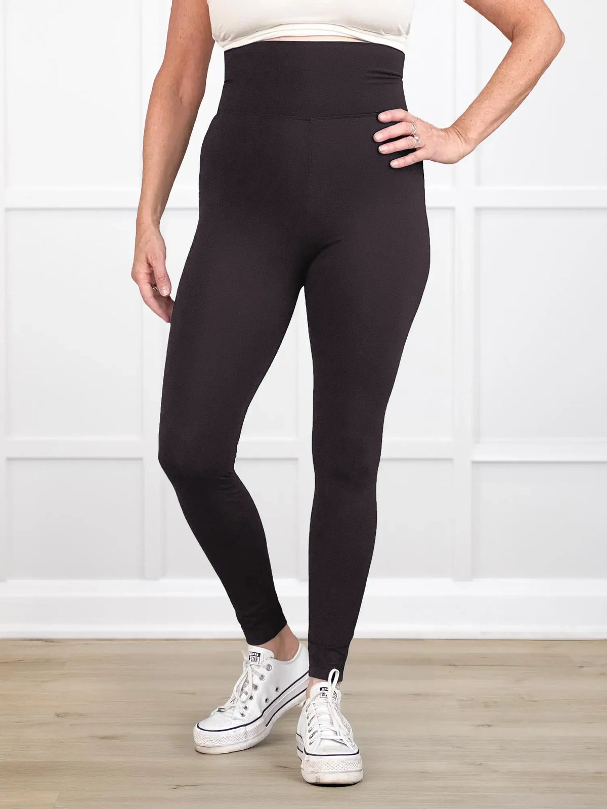 Person wearing black leggings with white sneakers on a light wooden floor and white wall background 