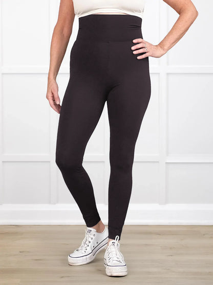 Person wearing black leggings with white sneakers on a light wooden floor and white wall background 