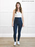 Woman wearing navy leggings and a white top in a room with white paneled walls. 