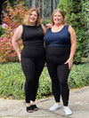 Miik models Bri and Kelly smiling while standing next to each other wearing the same outfit but with a different colour for the tank top. They are both wearing Miik's Lisa2 high waisted legging in blak, while Bri is wearing the Shandra tank in black and Kelly is wearing Alanis tank top in navy 