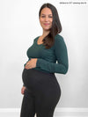 Miik model Adriana (five feet four, medium, pregnant) smiling in front of a white wall wearing Miik's Lisa2 high waited legging in charcoal 